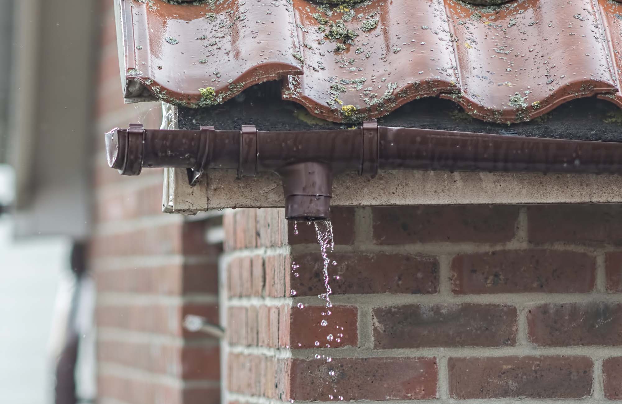 Broken gutter missing a downpipe. House guttering repair leaking rain water. Drainage problem with brown UPVC pipe in Birstall